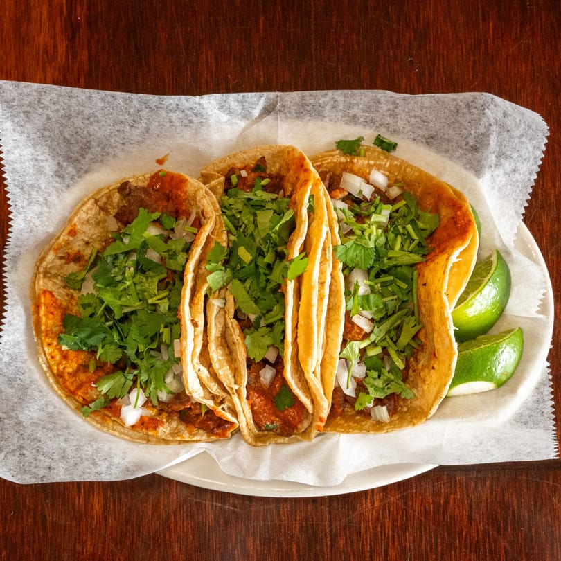 Three Tacos A La Diabla tacos with meat, cilantro, and onions, served with lime wedges.