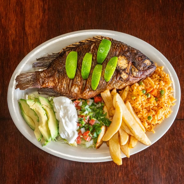Whole fried fish with lime slices, rice, french fries, avocado, sour cream, and pico de gallo.