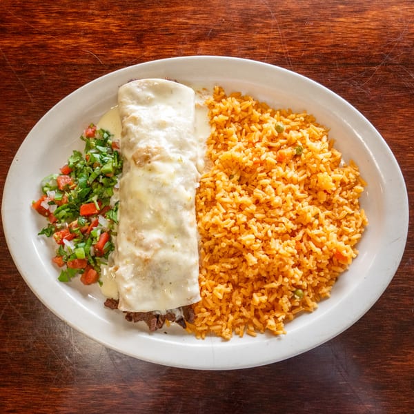A Tacos A La Diabla burrito covered in white cheese sauce, with rice and pico de gallo.
