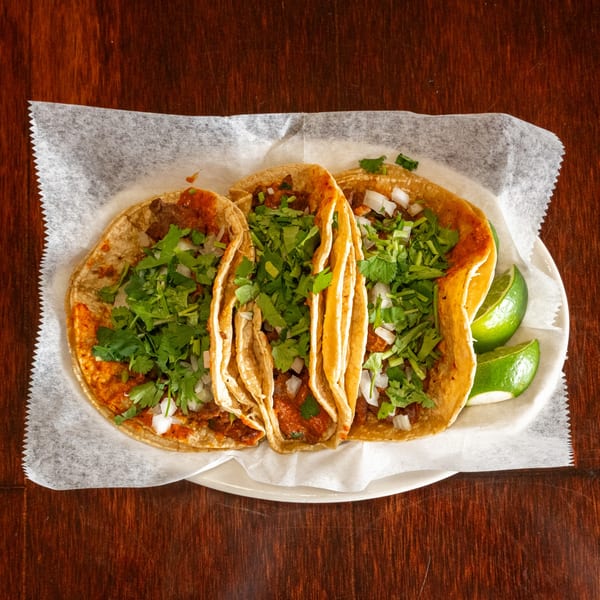 Three Tacos A La Diabla tacos with meat, cilantro, onions, and lime wedges on a white plate.