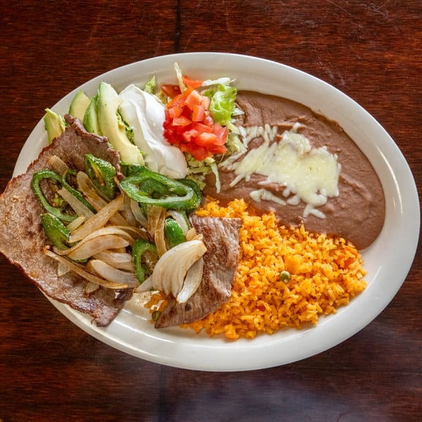 Carne asada with grilled onions and peppers, rice, refried beans, avocado, and sour cream.