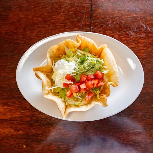A taco salad in a crispy tortilla bowl, topped with lettuce, tomatoes, guacamole, sour cream, and cheese.