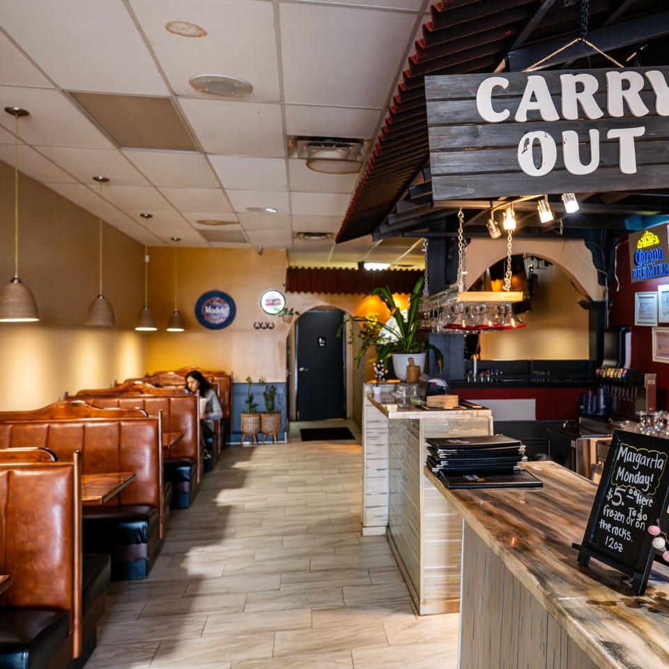 Interior of Tacos A La Diabla restaurant with booths, a bar, and a "Carry Out" sign.