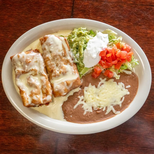 Two chimichangas with cheese sauce, refried beans, guacamole, sour cream, and pico de gallo.
